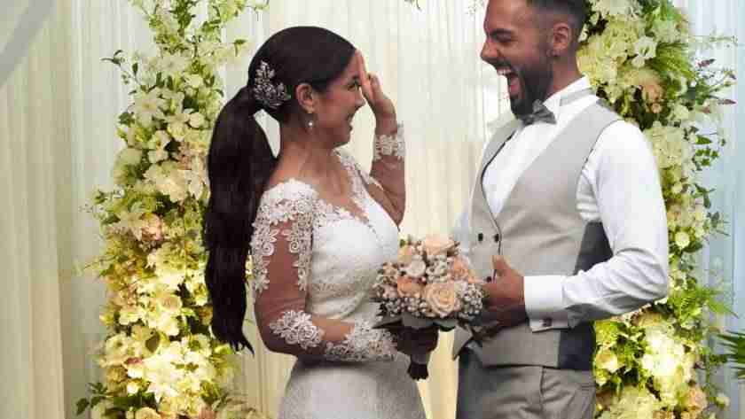 Bride and groom stand in front of floral backdrop celebrating small weddings and their wedding day